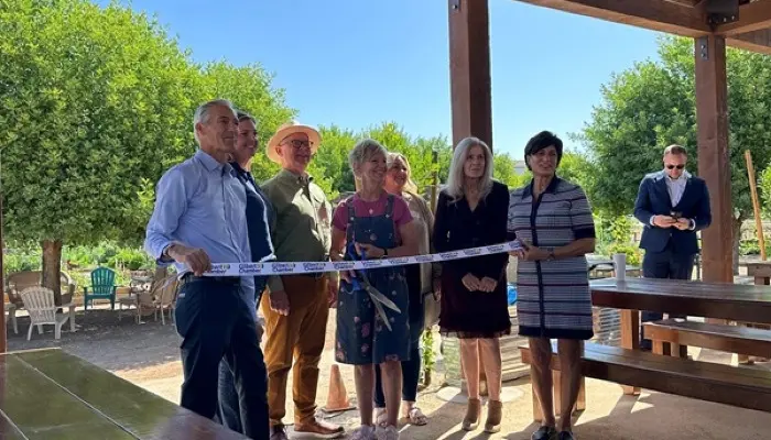 Crowd gathers around a ribbon for a ribbon cutting event. 